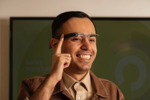 Ilustracja przedstawia, osoba, która dotyka przycisku, nosi specjalne okulary Envision, umożliwiające włączenie trybu zwiększającego kontrast na ekranie.