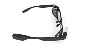 Ilustracja przedstawia okulary, które są wykonane z lekkiego i wytrzymałego materiału, a ich kształt jest oparty na klasycznych okularach, z jednym szkłem na każde oko. Na prawym okularze znajduje się mały ekran wyświetlający informację, a także kamera i mikrofon.