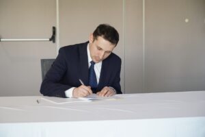 Na zdjęciu prezes Leszek Chojnicki, podpisujący Partnerstwo na rzecz dostępności. Siedzi On przy dużym stole, ubrany jest w ciemny garnitur.